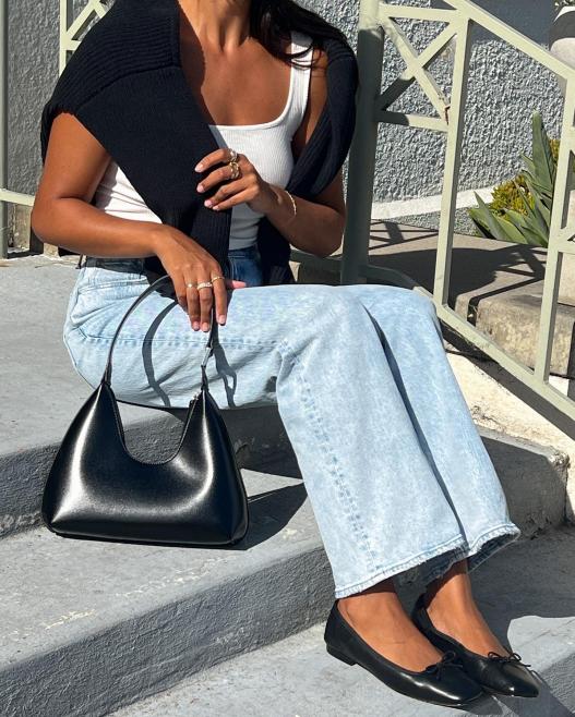 A-person-sitting-on-outdoor-steps,-wearing-light-blue-jeans,-black-flats,-and-holding-a-Freya-black-handbag.jpg